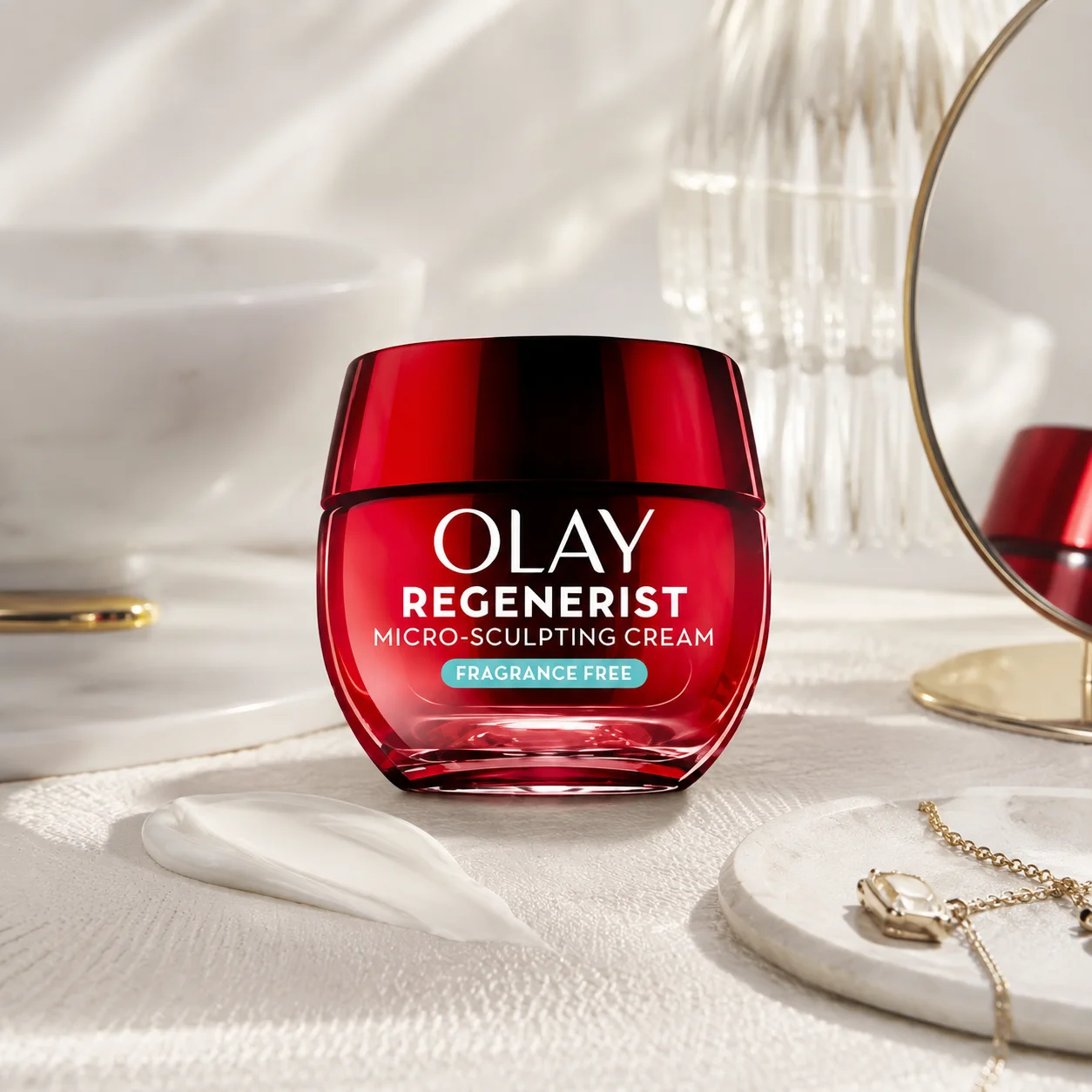 Olay Regenerist Micro-Sculpting Cream jar with red packaging displayed on a marble counter with a cream swatch, mirror, and jewelry in the background.